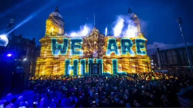 A historic building in Hull lit up with giant words "We are Hull", with crowds in the foreground