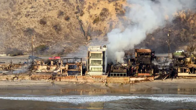 A single white three-floors property remains standing on the Maliby water front as all other houses next to it have been burned to the ground. White smoke billows from one home to the right of the frame