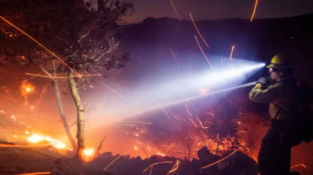 The wind whips embers while a firefighter battles the fire in the Angeles National Forest near Mt. Wilson as the wildfires burn in the Los Angeles area, during the Eaton Fire in Altadena