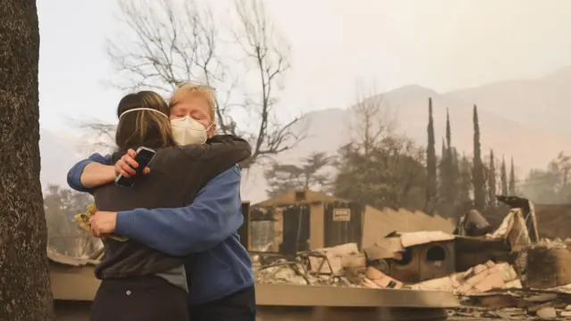 Two women hug in front of a burnt-out building