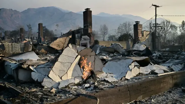 The foundations of a burned out home can be seen with flames still visible in a pile of white debris