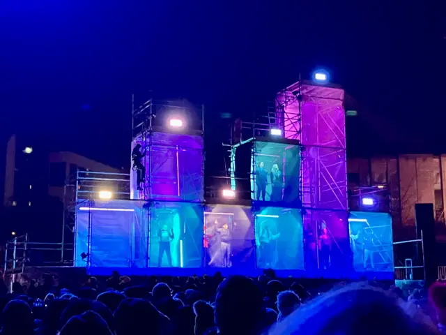 People in large illuminated cubes perform on stage