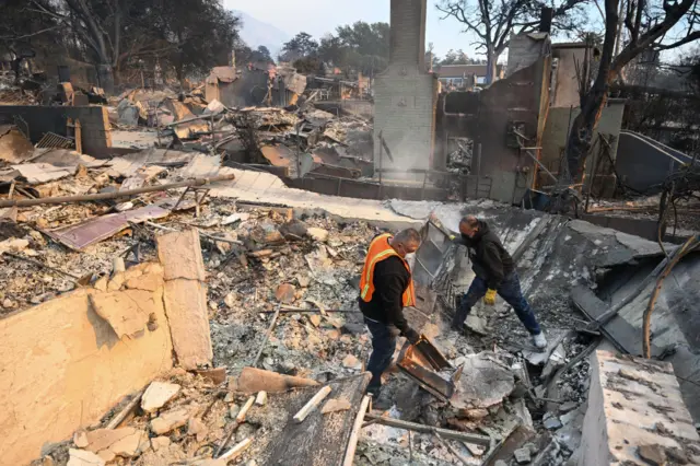 Two men in masks sort through rubble which was once a home