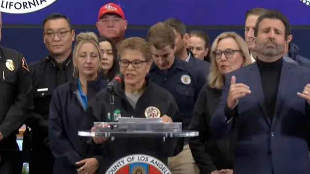 Los angeles mayor Karen Bass on stage as she delivers wildfires briefing wearing a blue jacket with county logo as other officials surround her