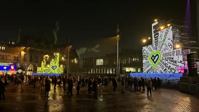 Hundreds of people in a square adorned with lights