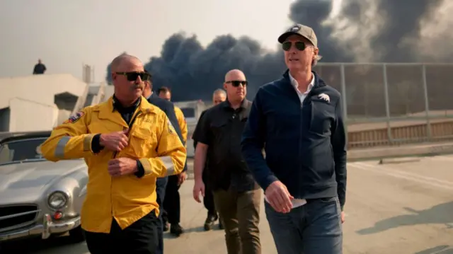 Gavin Newsom walks in Palisades as fire burns in the background