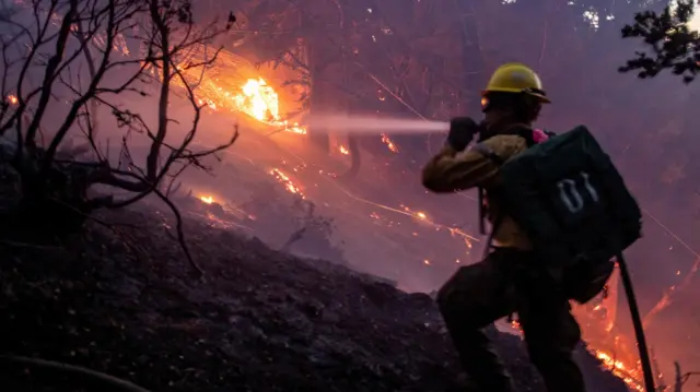 The wind whips embers while a firefighter battles the fire in the Angeles National Forest near Mt. Wilson