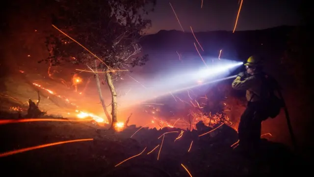 The wind whips embers while a firefighter battles the fire in the Angeles National Forest