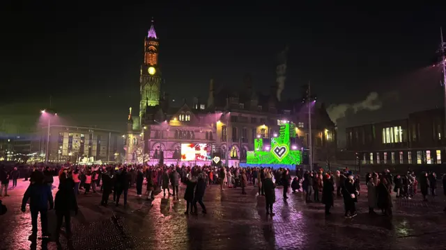 Hundreds of people in a square adorned with lights