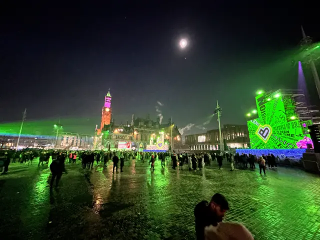 Hundreds of people in a square adorned with lights