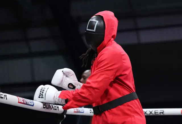 Deevorn Miller dressed as a Squid Game guard enters the ring