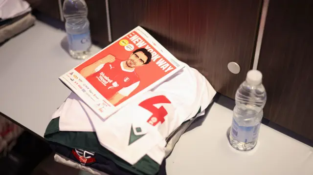 A look inside the Bolton dressing room with a shirt and matchday programme on the bench