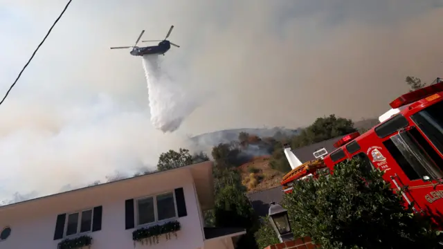 A helicopter makes a drop as smoke billows from the Palisades Fire at the Mandeville Canyon