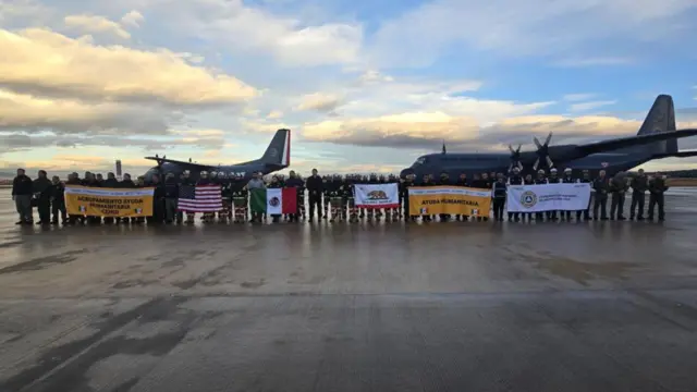 Mexican firefighters posing for a photograph wild holding flags and banners in front of two planes