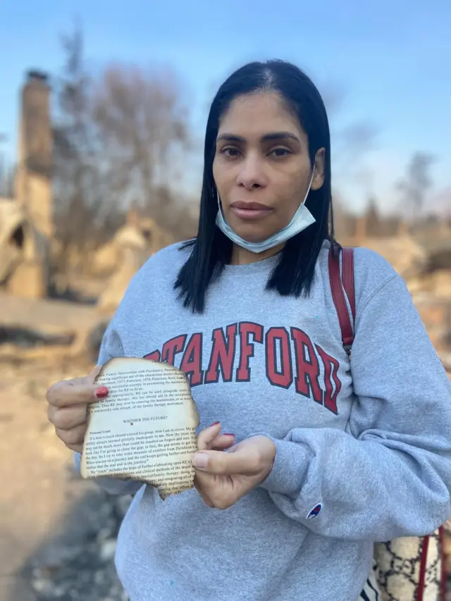 A woman holds a burnt piece of a book that survived the fire