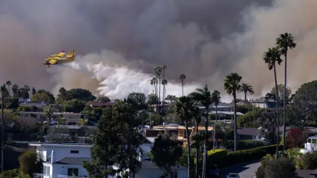 A Super Scooper drops ocean water on a hillside as the Palisades fire rages