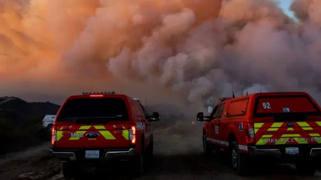 Torrance Fire Department vehicles parked as smoke billows from the Palisades Fire, threatening homes in the Brentwood area