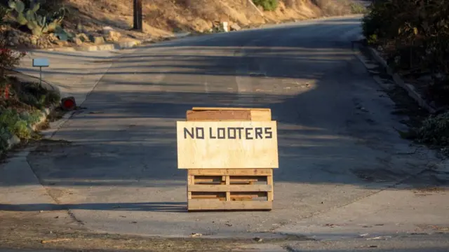 A "no looters" sign is placed on a road after residents fled from the Eaton Fire