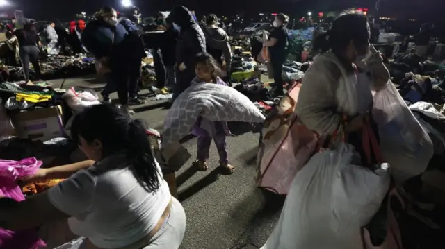 People, including a child, carrying blankets and bedding at a distribution centre at Santa Anita Park in Arcadia, Pasadena