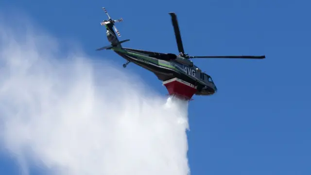 A helicopter drops water during the Palisades Fire near the Mandeville Canyon area of Los Angeles, California, US, on Sunday, Jan. 12, 2025