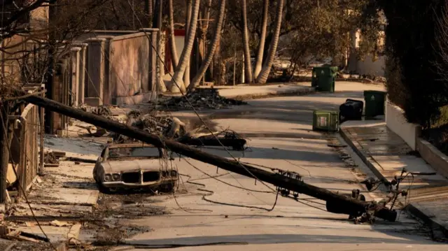 Street scene showing a downed power line, a burned out car and debris across the road