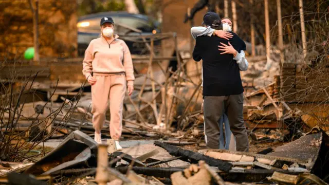 A man hugs a family member and cries while viewing the remains of his home burned in the Eaton fire in the Altadena area of Los Angeles county,