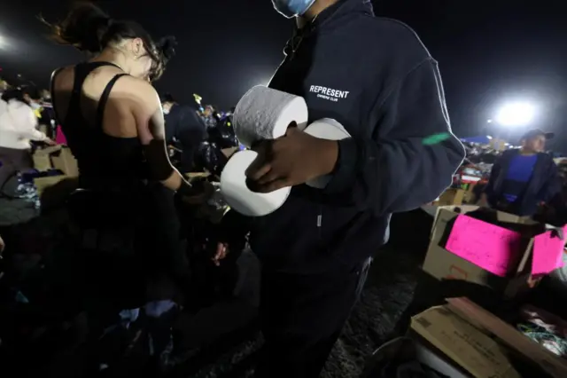 A person carrying three rolls of toilet paper at a distribution centre at Santa Anita Park in Arcadia, Pasadena