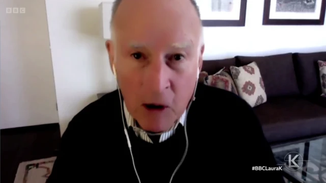 Jerry Brown, a former governor of California with earphones in speaking into a camera