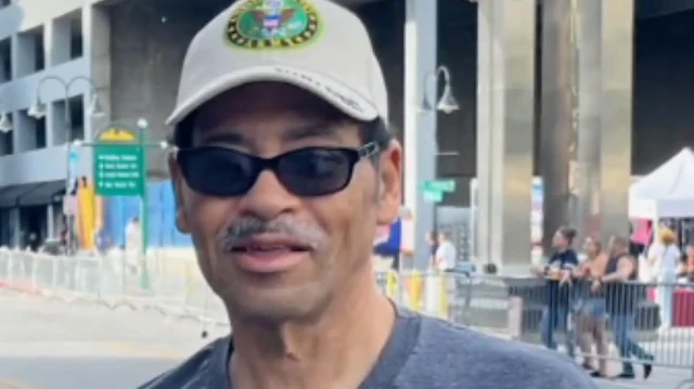 Headshot of Victor Shaw, wearing a cap and sunglasses with a street scene behind him