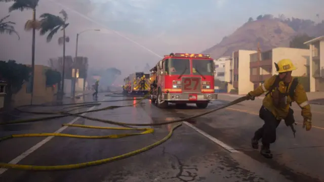 A firefighter drags a hose during the Palisades fire in Malibu