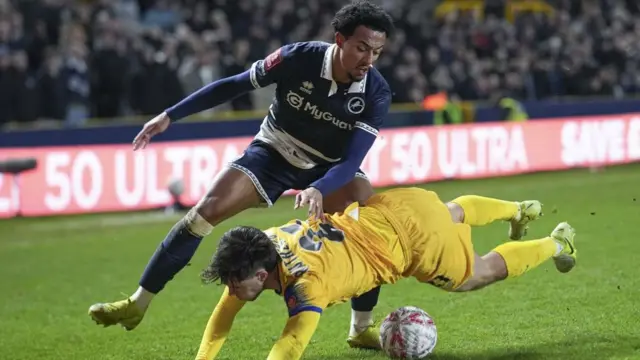 Dagenham's Oscar Rutherford takes a tumble under pressure from Millwall's Femi Azeez