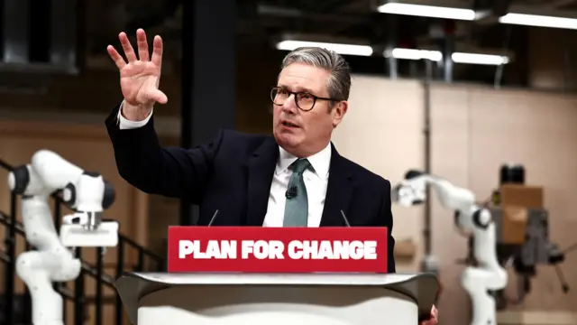 Starmer gestures at a podium which says 'plan for change'