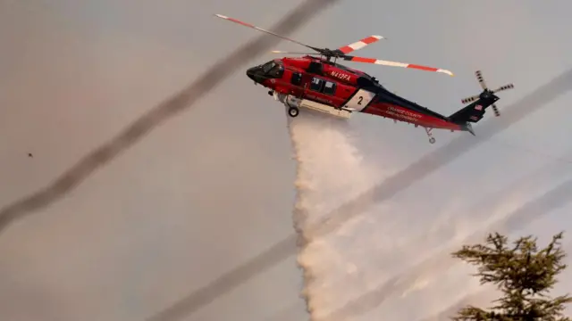 A helicopter drops water and fire retardant onto the Los Angeles area wildfires. The sky is relatively clear