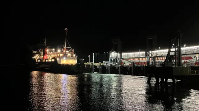 A ferry leaves the pier at Brodick Harbour The ferry and the pier are both illuminated in the dark.