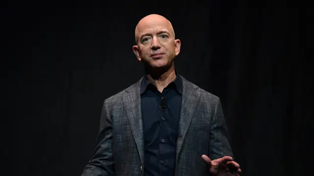 Jeff Bezos in front of a black background wearing a grey suit