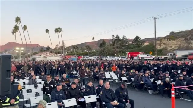 People in uniforms gather in folded chairs with palm trees in the background