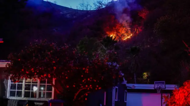 A hillside burns behind houses in the Mandeville Canyon neighbourhood during the aftermath of the Palisades Fire in the Pacific Palisades area of Los Angeles