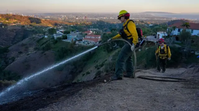 Firefighters from Oregon spray water over a hillside during the aftermath of the Palisades Fire in the Pacific Palisades area of Los Angeles, California, US, on Sunday, Jan. 12, 2025