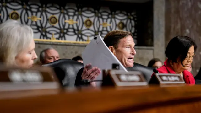 Blumenthal on dais, holding up stack of papers