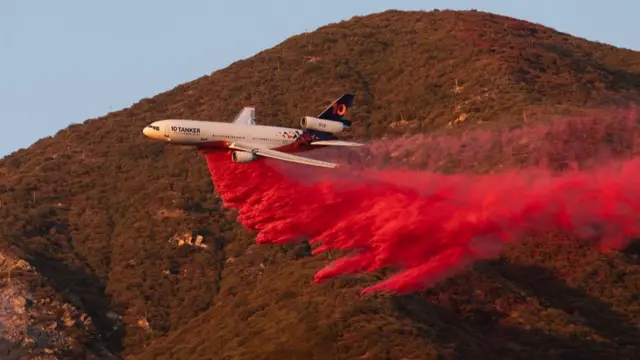 Hot pink gas coming out the bottom of a plane as it flies over a hill