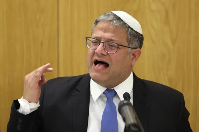 Ben-Gvir speaking passionately with one arm gesturing. He wears a black suit, blue tie, white shirt, and kippah