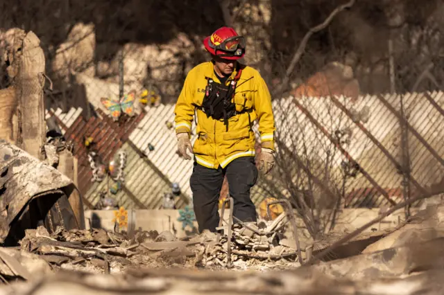 A firefighter looks through the rubble of a burned home in Altadena