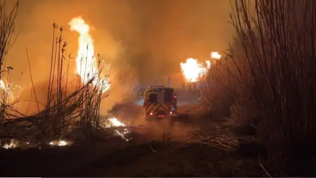 A fire truck surrounded by flames and an orange sky