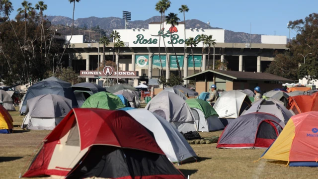 Tents housing first responders pitched on the grassy ground outside the Rose Bowl, visible in the background. The Los Angeles hills are also visible, with various greenery - including palms - in the far background