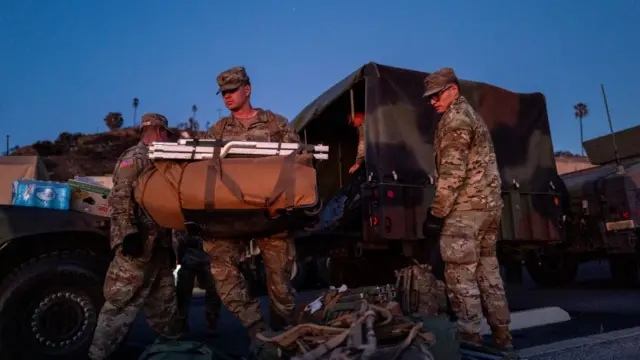 Three male National Guard members in military camouflage unloading equipment from the back of a truck in California.