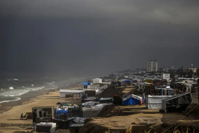 A dark and dismal day at the beach, with strong waves. Just a little bit back on the beach, as far as the eye can see, is rows and rows of tents