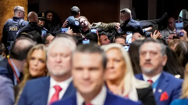 Security personnel remove a protester as Pete Hegseth speaks