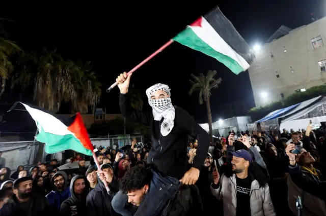 A man waves Palestinian flags as Palestinians react to news on a ceasefire deal with Israel, in Deir Al-Balah in the central Gaza Strip