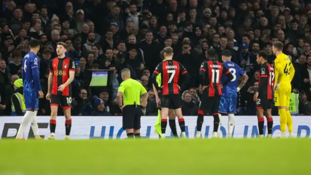 The referee reviewing the David Brooks incident on the monitor