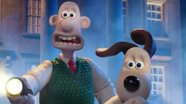 Wallace holds a hand torch alongside Gromit, surrounded by fog and Regency architecture